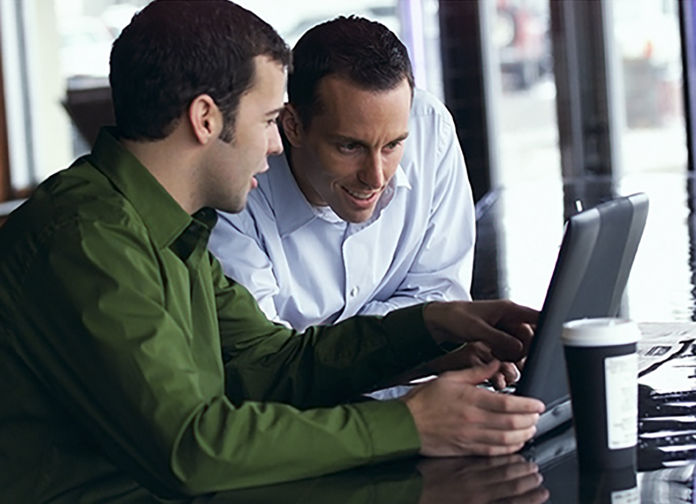 Two males sitting and looking at a laptop computer.