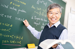 Male professor writing mathematic formulas on chalkboard.